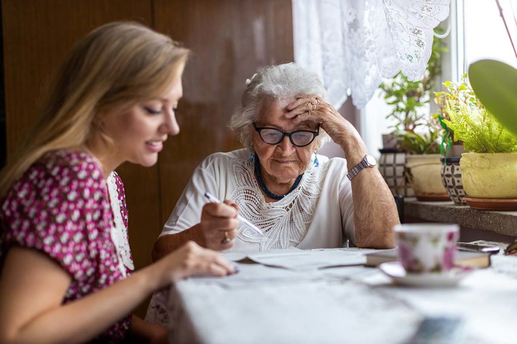a senior adult and a young woman review papers on coping strategies for caregivers