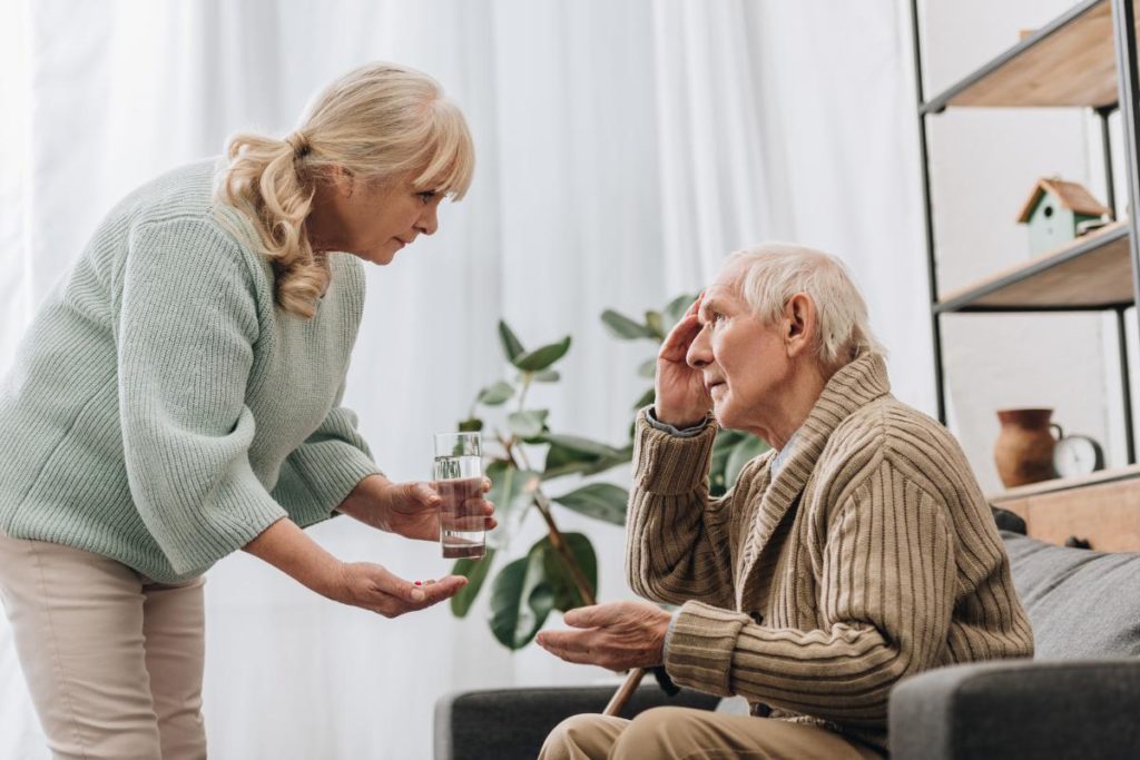 woman handing old man pills discussing things to do with someone who has alzheimers & talking about things to do with someone who has alzheimers