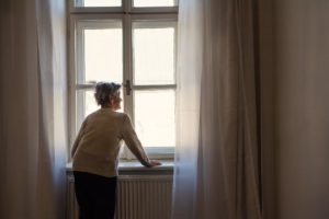 a person looking out of a window experiences Senior loneliness