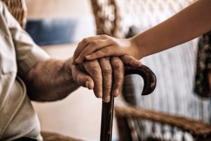 Caregiver's hand on elderly person's hand holding onto a cane while in respite care for seniors
