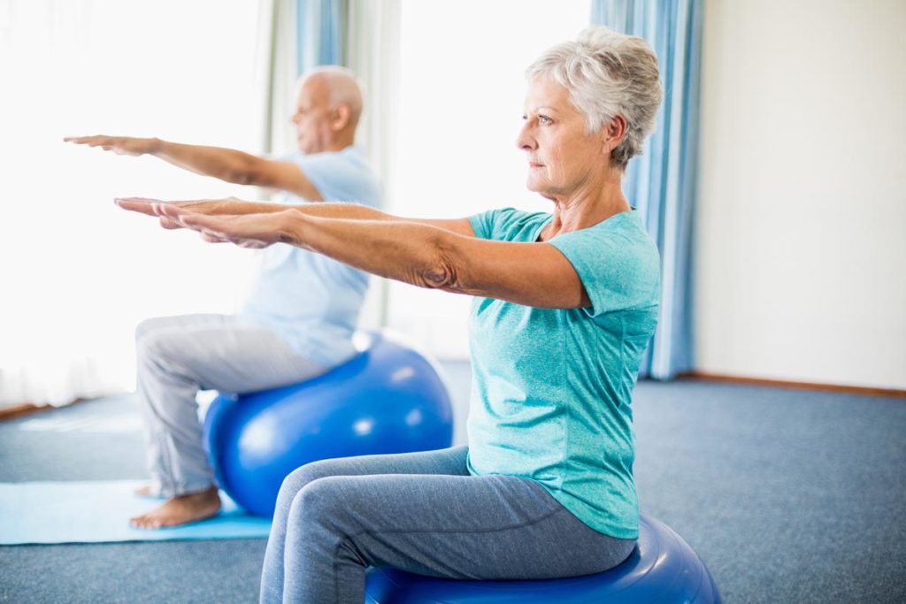 two people practice balance exercises for seniors on yoga balls
