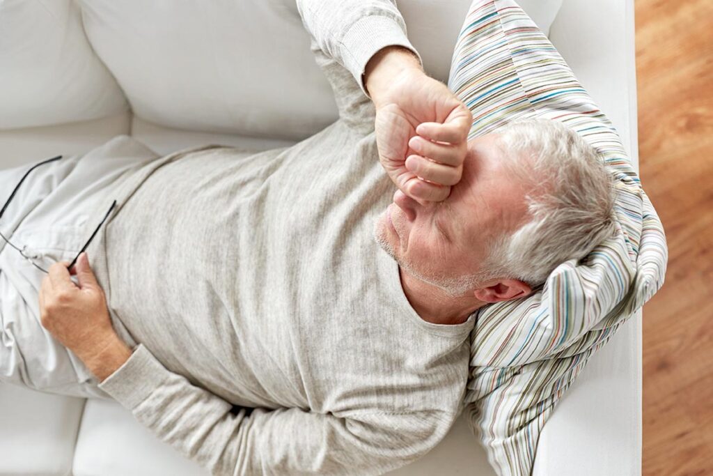 person lying on couch with headache while struggling with signs of pneumonia