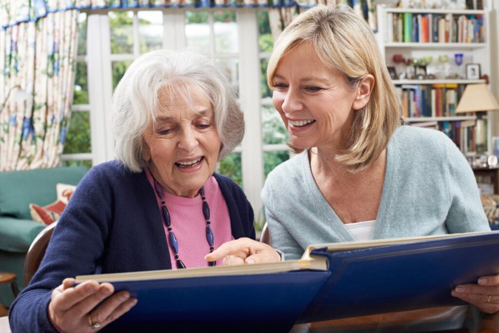 Elderly woman and caretaker looking at photo album while discussing if it's time for senior memory care