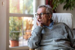 Older man gazing out of window while grappling with independent living challenges