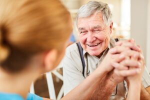 Happy senior man joining hands with caregiver while answering the question what is senior memory care