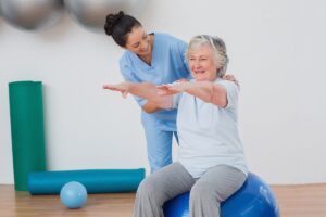Caregiver guiding senior through exercise ball routine while performing nursing home physical therapist duties