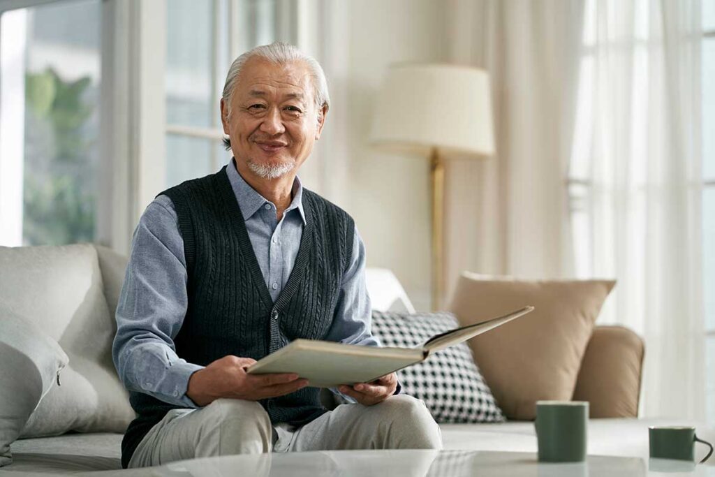 Man smiling while sitting on comfortable couch reading book after answering the question what is senior independent living