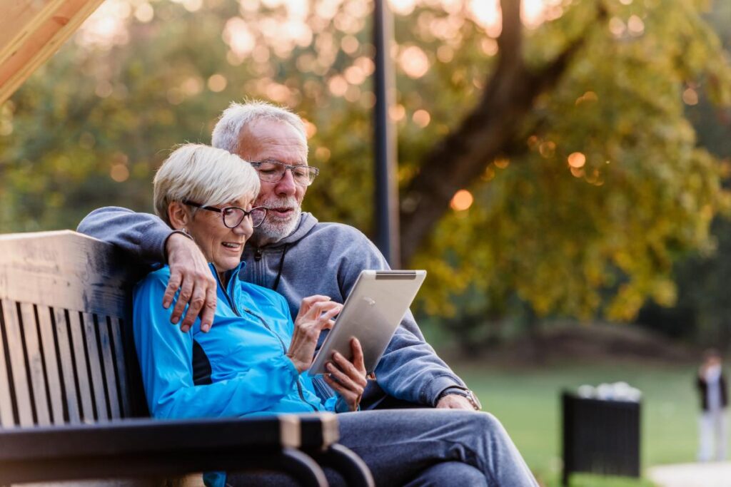 senior couple sitting on park bench while using tablet to research senior independent living costs in Austin TX