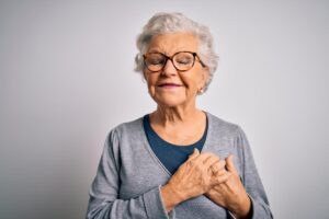 senior woman smiling with eyes closed and hands over heart while contemplating what is memory care like in Austin TX
