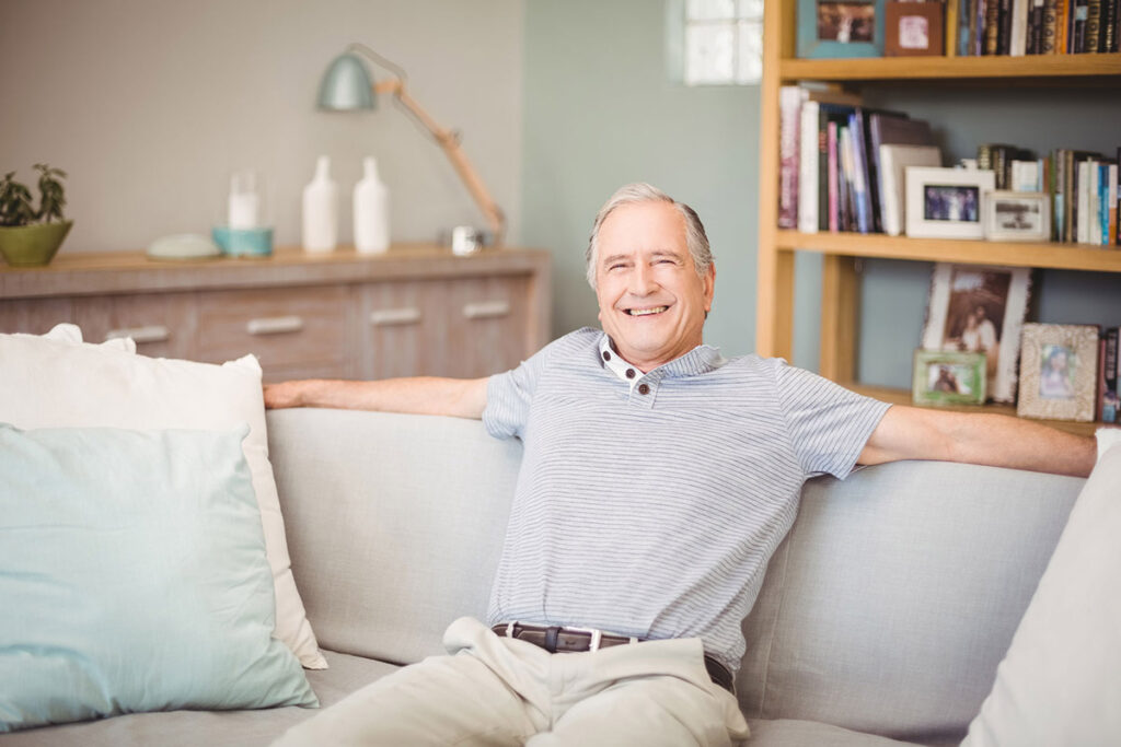 person smiling while sitting on comfortable couch after covering the costs of senior assisted living