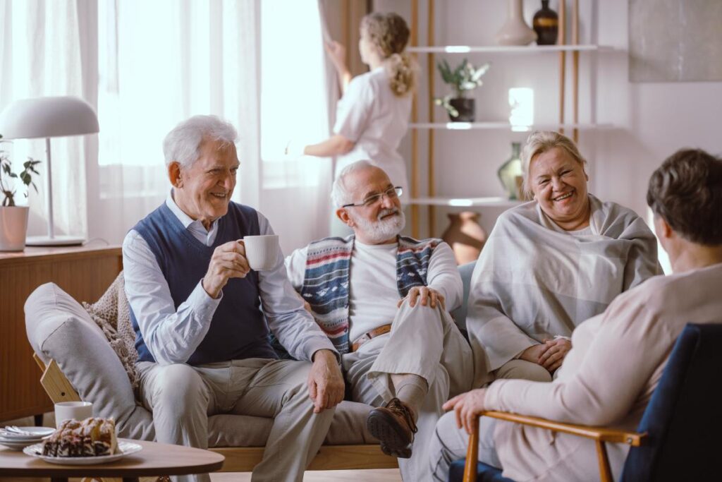 older adults smiling while gathered in living area discussing how respite care connects families and caregivers