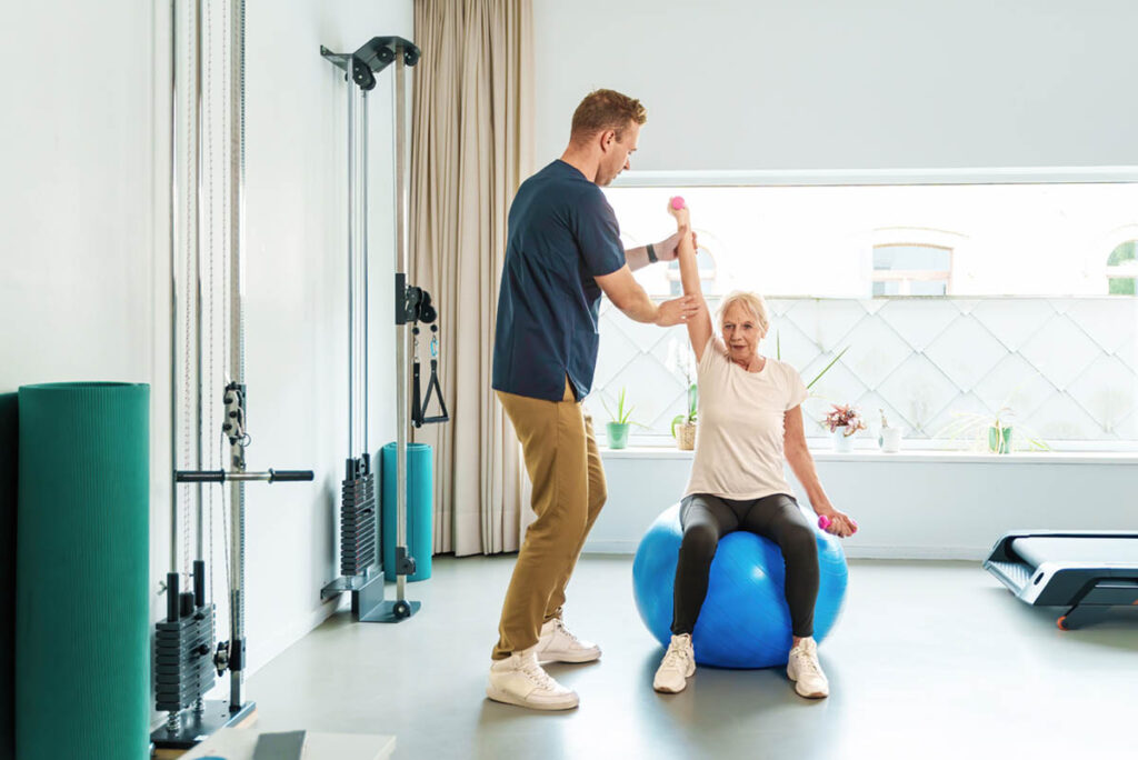 trainer helping senior woman with exercise ball routine as part of wellness programs in senior living